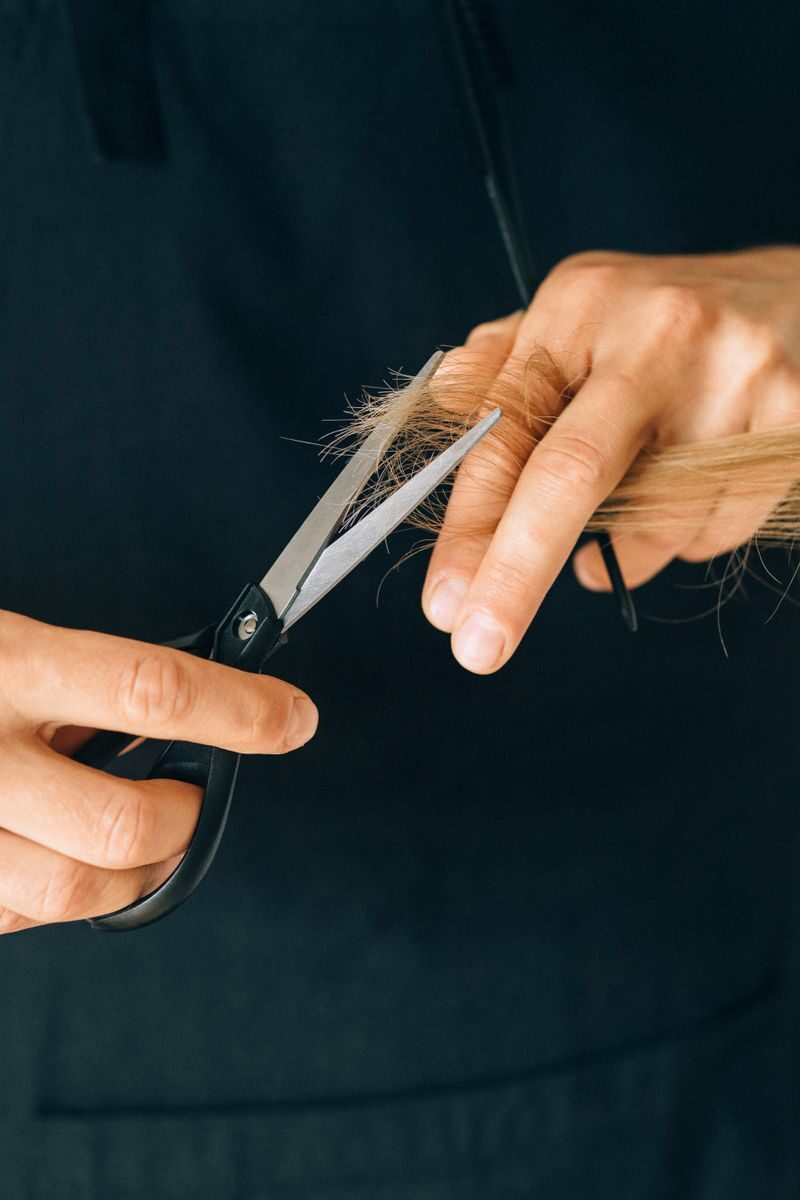 Detailed close-up of hands holding scissors, trimming hair in a salon setting.