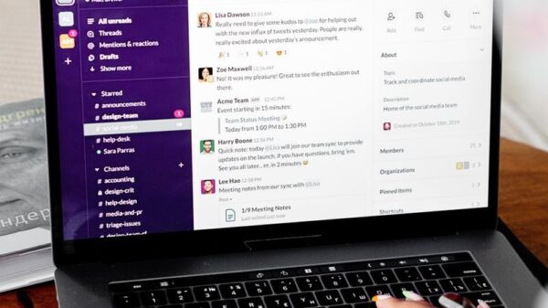 Close-up of hands typing on a laptop displaying Slack for remote communication.