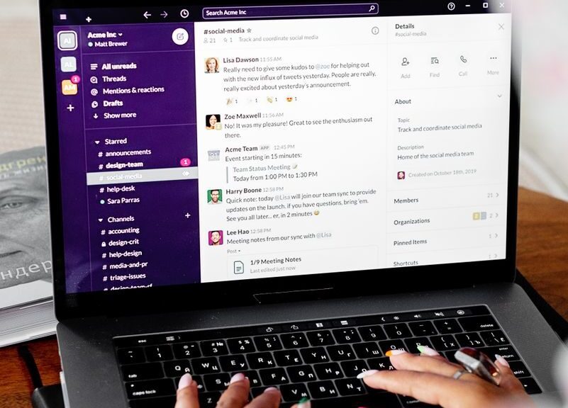 Close-up of hands typing on a laptop displaying Slack for remote communication.