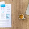 Top view of a desk with resume, coffee cup, and laptop on a wooden surface, ideal for business concepts.