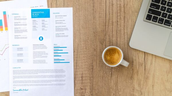 Top view of a desk with resume, coffee cup, and laptop on a wooden surface, ideal for business concepts.