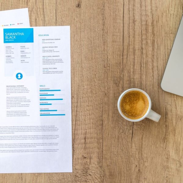 Top view of a desk with resume, coffee cup, and laptop on a wooden surface, ideal for business concepts.