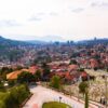 Aerial view of Sarajevo, showcasing cityscape, red rooftops, and distant mountains.