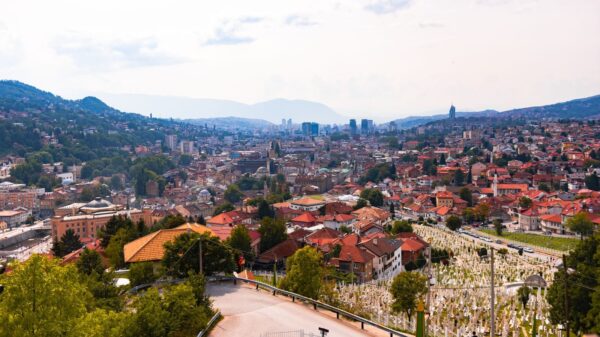 Aerial view of Sarajevo, showcasing cityscape, red rooftops, and distant mountains.