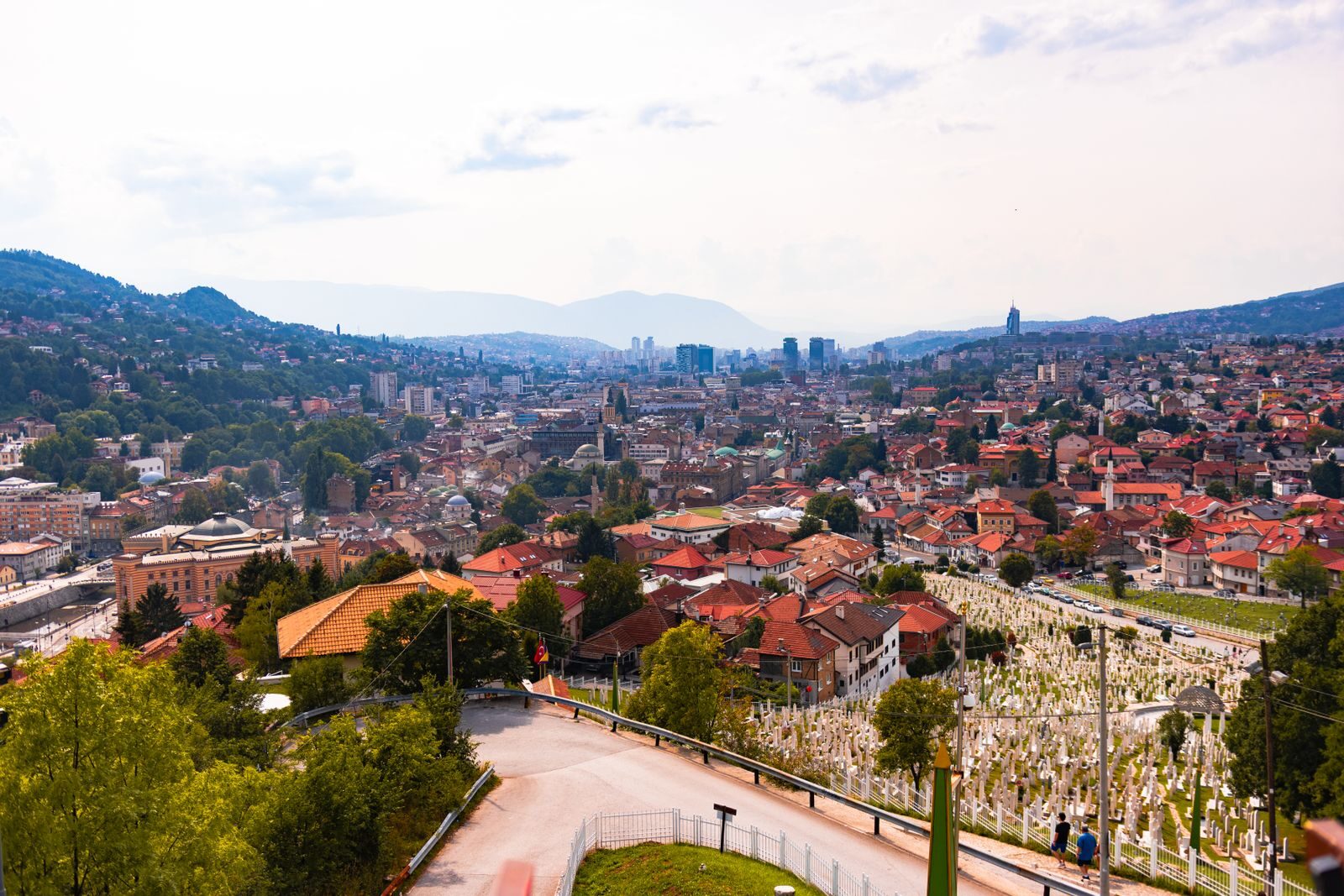 Aerial view of Sarajevo, showcasing cityscape, red rooftops, and distant mountains.
