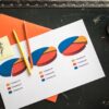 Colorful pie charts on paper with office supplies on a desk, illustrating financial data analysis.