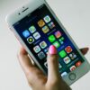 Close-up of a hand holding a smartphone displaying various apps on the screen.