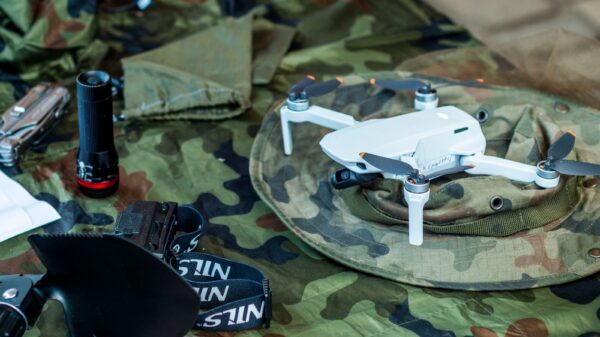 Compact white drone on camouflage gear, surrounded by flashlight and tools.