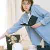 A young woman multitasks with a phone call and notebook in a casual home office setting.
