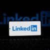 Smartphone showing LinkedIn logo with keyboard and large background logo, business theme.