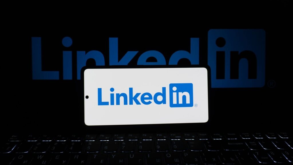 Smartphone showing LinkedIn logo with keyboard and large background logo, business theme.