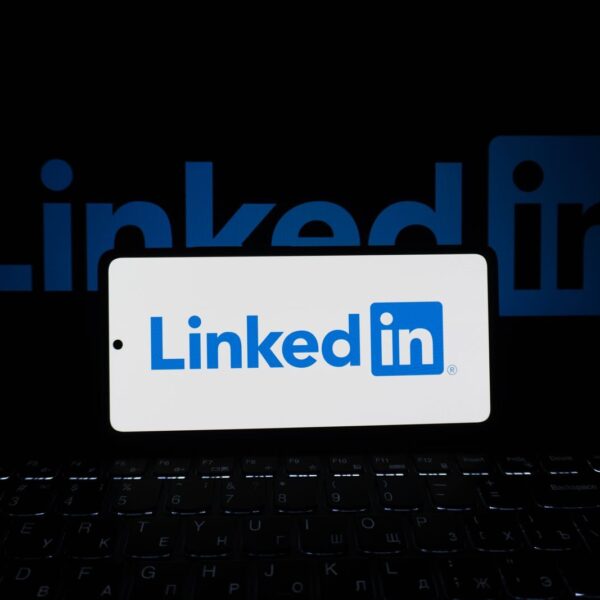 Smartphone showing LinkedIn logo with keyboard and large background logo, business theme.
