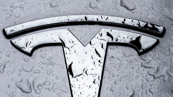 Metallic Tesla logo covered in raindrops, showcasing sleek design.