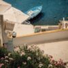 A blue boat moored in clear water beside a white terrace with flowers.