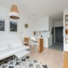 Comfortable couch with cushions placed in modern living room near kitchen zone with wooden counter and chairs
