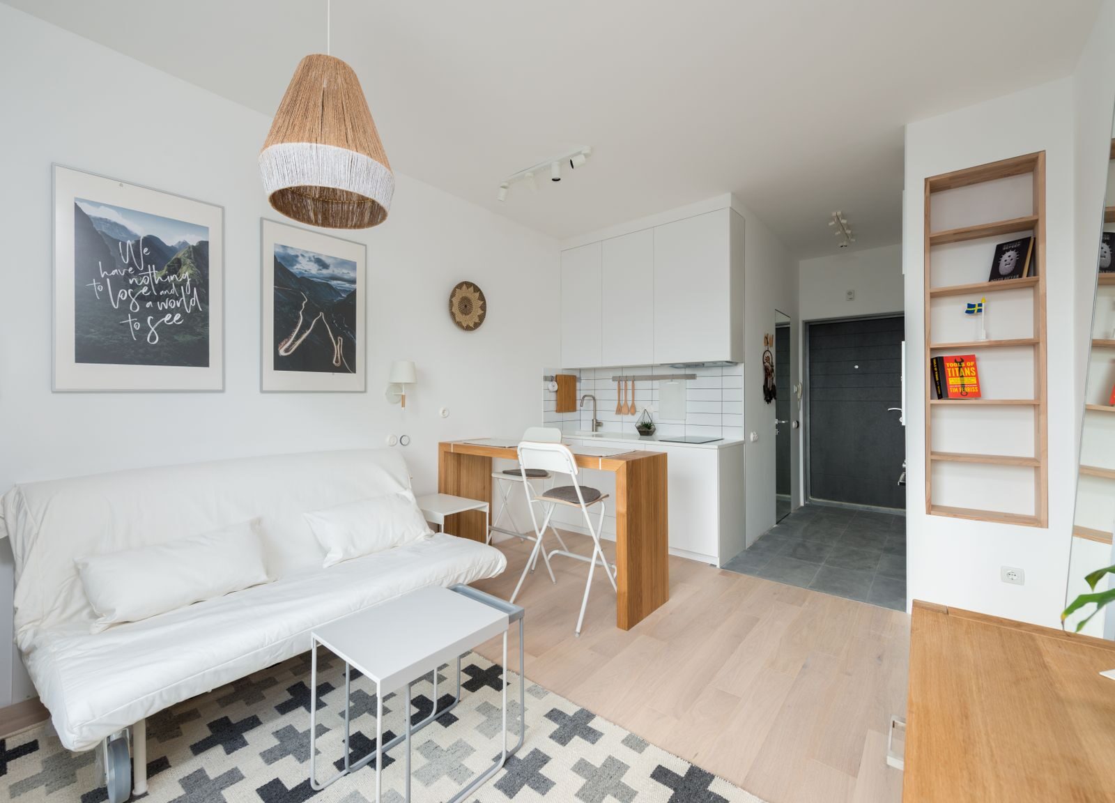 Comfortable couch with cushions placed in modern living room near kitchen zone with wooden counter and chairs