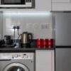 Stylish modern kitchen with stainless steel appliances and red accents, highlighting a washing machine, fridge, and countertop electronics.