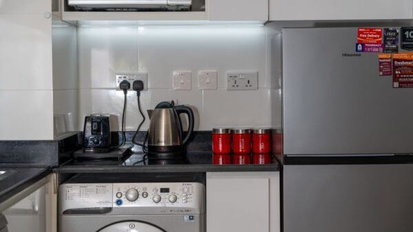 Stylish modern kitchen with stainless steel appliances and red accents, highlighting a washing machine, fridge, and countertop electronics.