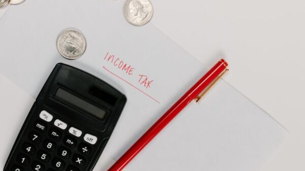 Calculator, pen, and coins on an envelope labeled 'Income Tax' for tax preparation.