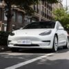 A sleek white Tesla Model 3 parked on a city street under trees, showcasing modern automotive design.