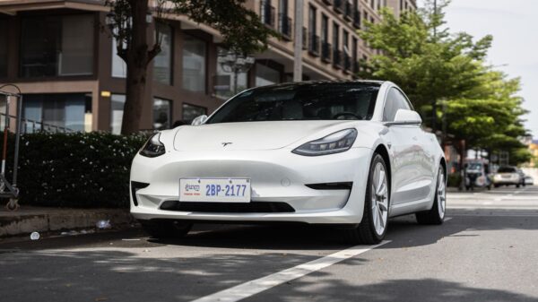 A sleek white Tesla Model 3 parked on a city street under trees, showcasing modern automotive design.