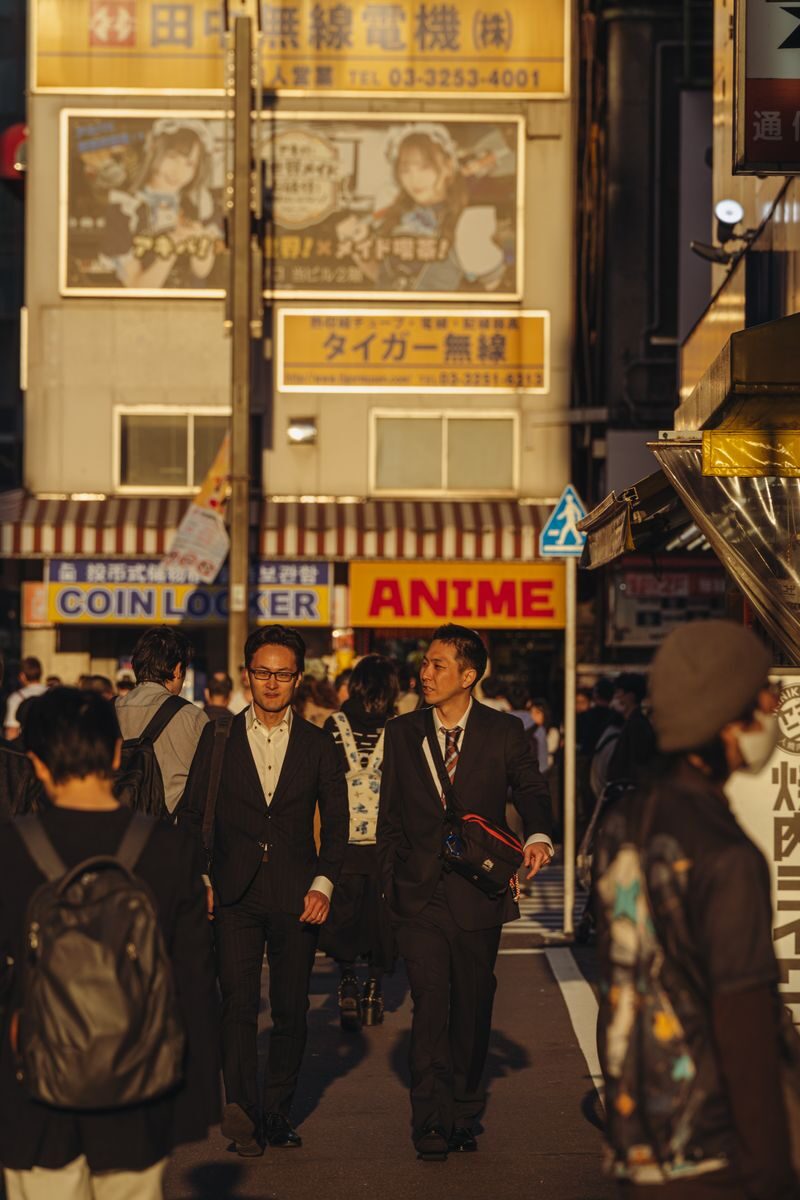 Crowded street in Tokyo with business people and anime signs in warm daylight.