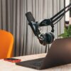 Modern podcasting studio with mic, headphones, laptop, and smartphone on a wooden table.