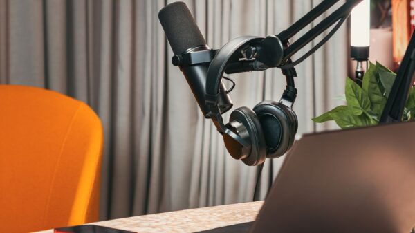 Modern podcasting studio with mic, headphones, laptop, and smartphone on a wooden table.