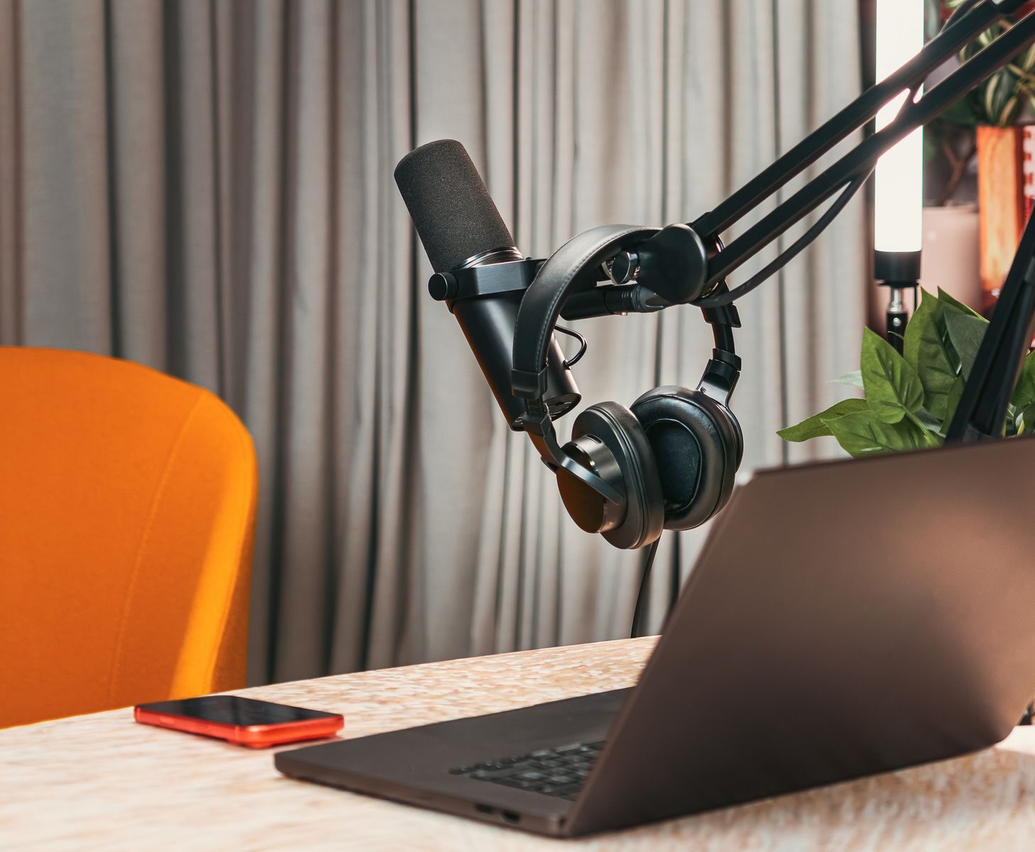 Modern podcasting studio with mic, headphones, laptop, and smartphone on a wooden table.