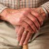 A detailed image of elderly hands clasping a wooden cane, symbolizing aging and support.
