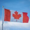 A vibrant Canadian flag waving in the breeze against a bright blue sky, symbolizing national pride.