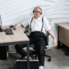 Senior man in a white shirt and headphones relaxing in an office chair by a desk.
