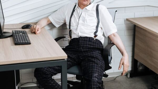 Senior man in a white shirt and headphones relaxing in an office chair by a desk.