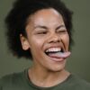 Close-up of a smiling woman with afro hair making a playful expression against a green background in a studio.