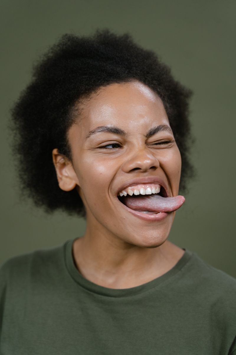 Close-up of a smiling woman with afro hair making a playful expression against a green background in a studio.