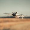 White drone flying over a golden field on a clear day, showcasing modern technology.
