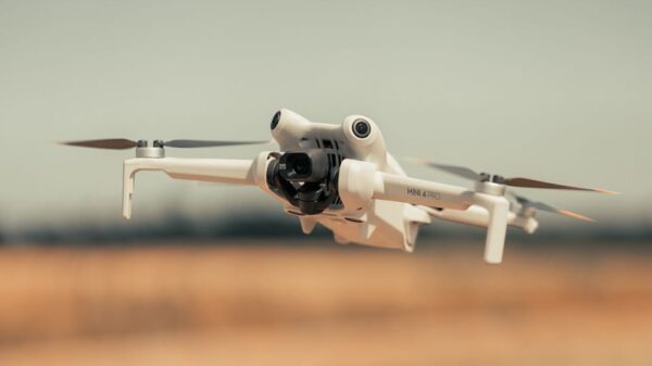 White drone flying over a golden field on a clear day, showcasing modern technology.