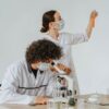Two scientists in protective gear working on a laboratory experiment with glassware and a microscope.
