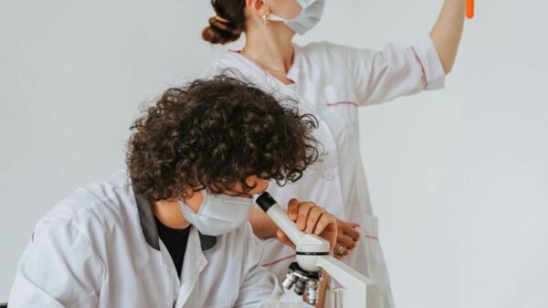 Two scientists in protective gear working on a laboratory experiment with glassware and a microscope.