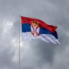 Serbian flag on pole against overcast sky, symbolizing national pride.