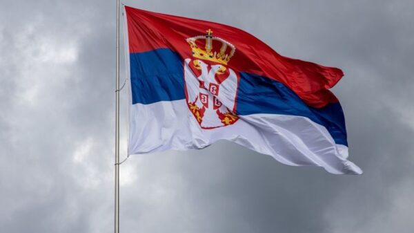 Serbian flag on pole against overcast sky, symbolizing national pride.