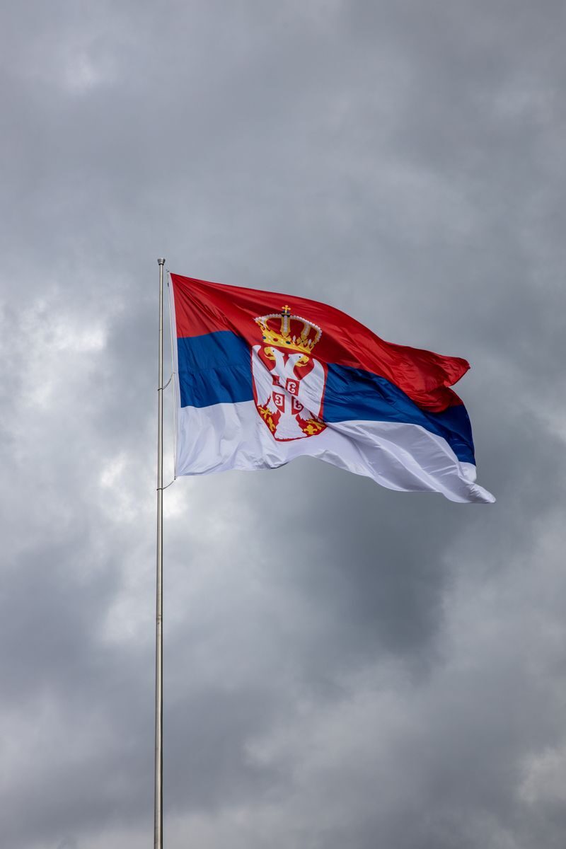 Serbian flag on pole against overcast sky, symbolizing national pride.