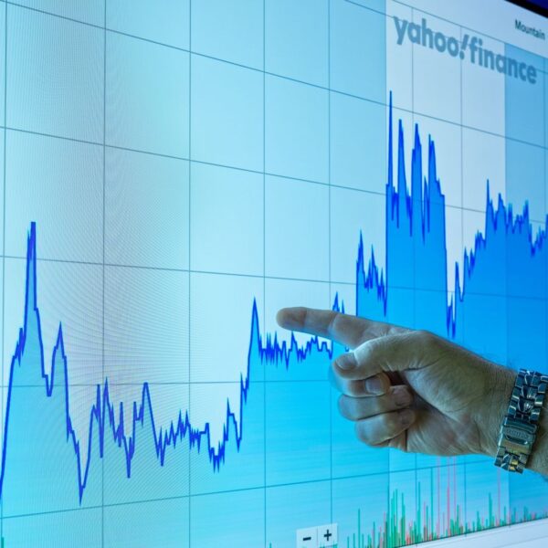 A hand points to a financial graph on a large screen, indicating market trends.