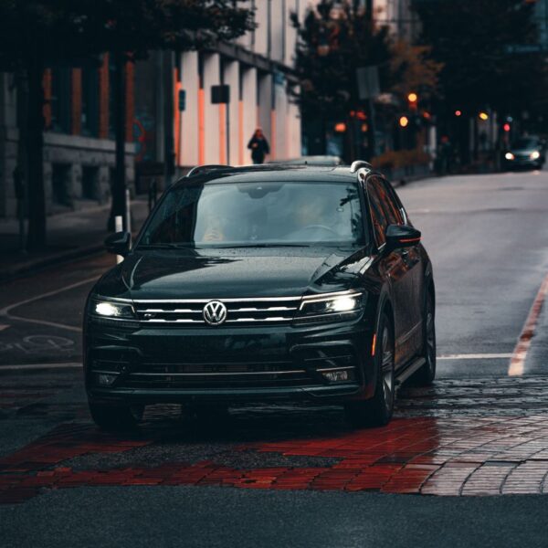 A black Volkswagen car driving on a wet urban street, emphasizing transportation in rainy weather.