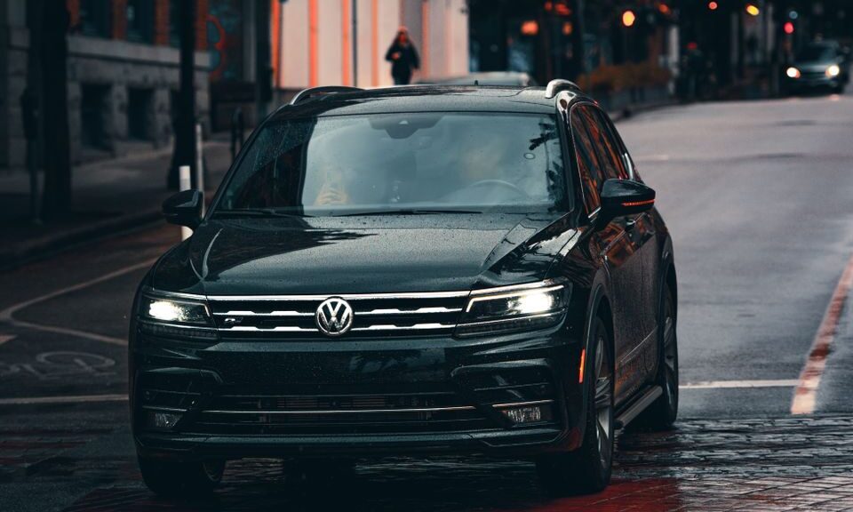 A black Volkswagen car driving on a wet urban street, emphasizing transportation in rainy weather.