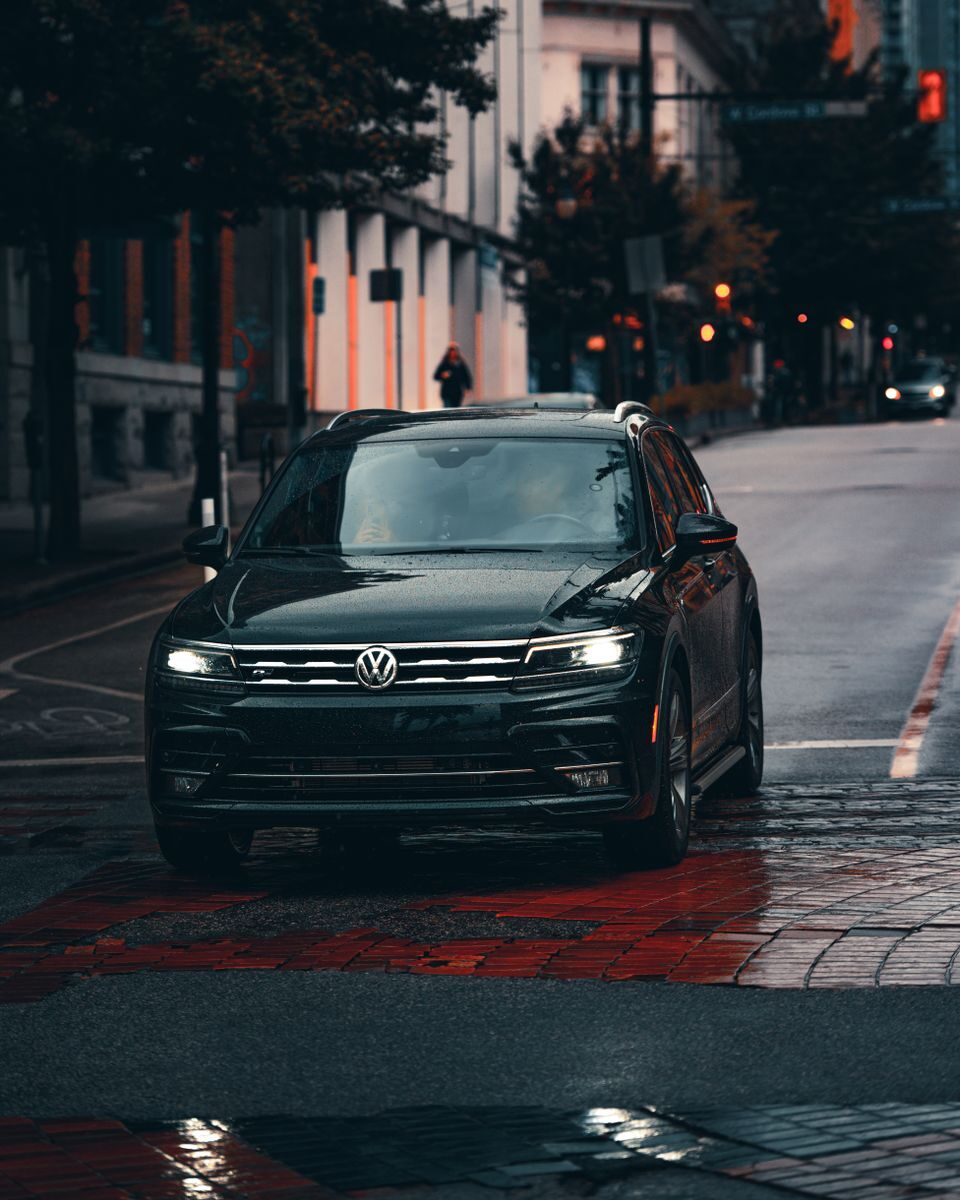 A black Volkswagen car driving on a wet urban street, emphasizing transportation in rainy weather.