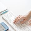 Close-up of a hand typing on a white keyboard with office supplies nearby, conveying a modern workspace.