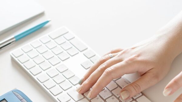 Close-up of a hand typing on a white keyboard with office supplies nearby, conveying a modern workspace.