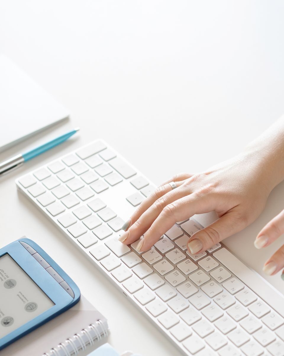 Close-up of a hand typing on a white keyboard with office supplies nearby, conveying a modern workspace.