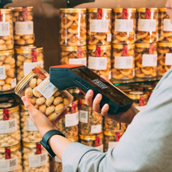 Individual scanning QR codes on jars in a store with a handheld device.